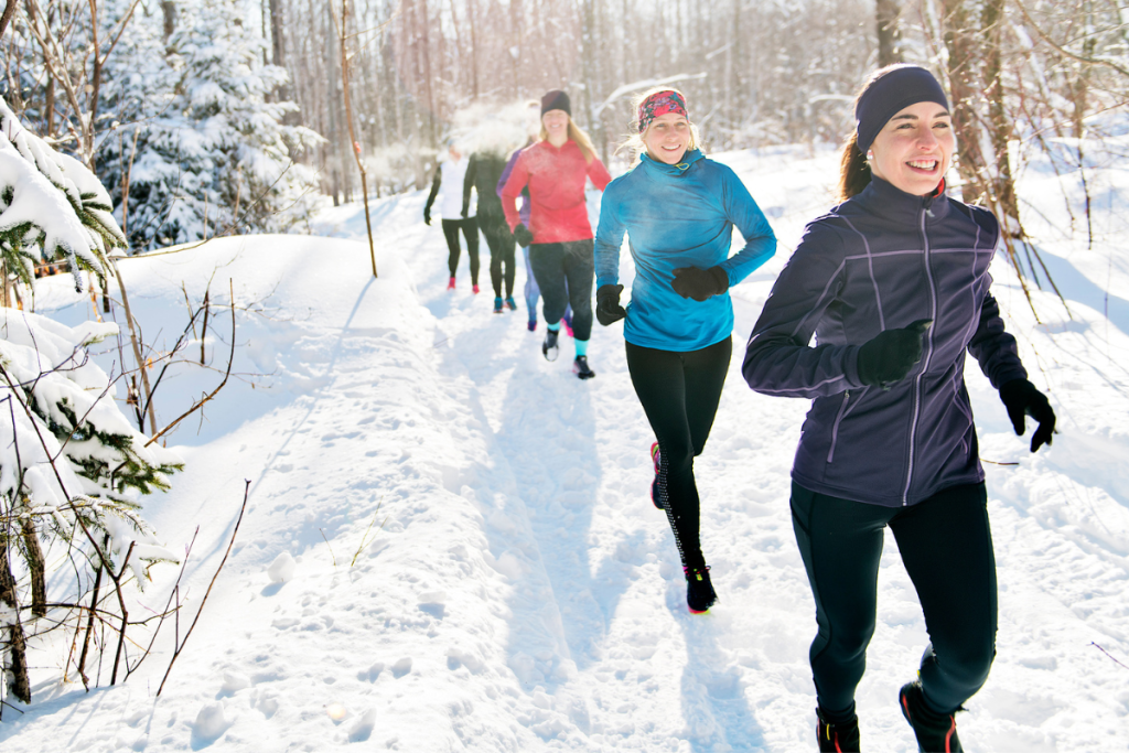 Female runners who are running in the snow on a path in the forest.